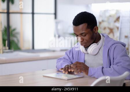 Black man using digital tablet on kitchen at home, working office work remotely typing text, African american freelancer using notepad computer Stock Photo