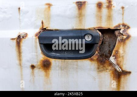 Rust and cracked paint next to door handle on an old rusty car close-up. Stock Photo