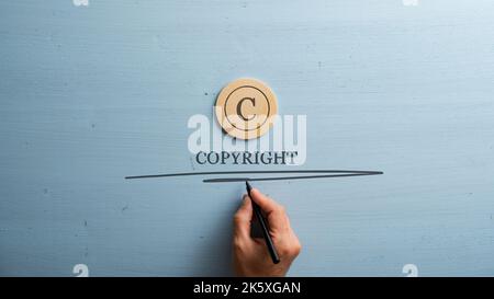 Circled letter C on a wooden cut circle with male hand writing a Copyright word under it. Over wooden blue background. Stock Photo