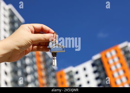 Real estate agent, home keys in female hand on background of new building. Byung apartment or renting property Stock Photo