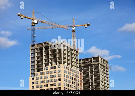 Tower cranes and unfinished buildings on background of blue sky with white clouds. Housing construction, apartment blocks in city Stock Photo