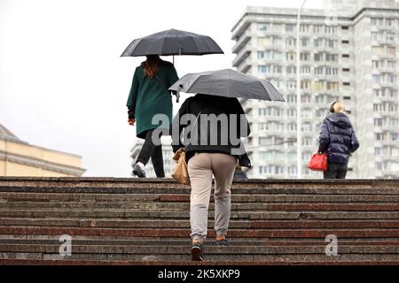 People with umbrellas walking up the steps on city buildings background. Rain in autumn city Stock Photo