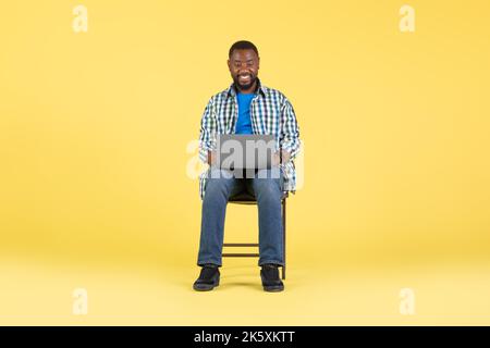 Happy African American Guy Using Laptop Sitting Over Yellow Background Stock Photo