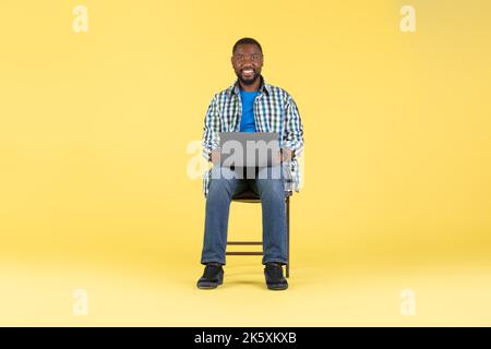 Cheerful Black Man Using Laptop Working Online On Yellow Background Stock Photo