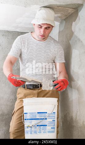 Dolyna , Ukraine April 11, 2022:The master works with lime plaster, leveling the wall with a spatula and lime plaster, repairing work on leveling the Stock Photo