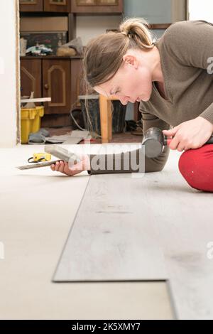 Quartz vinyl flooring and installation, a woman knocks a rubber hammer on the floor locks, repairs in the house. Stock Photo