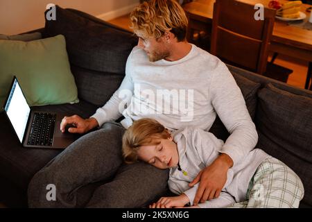 White father and son using laptop while resting on sofa at home Stock Photo