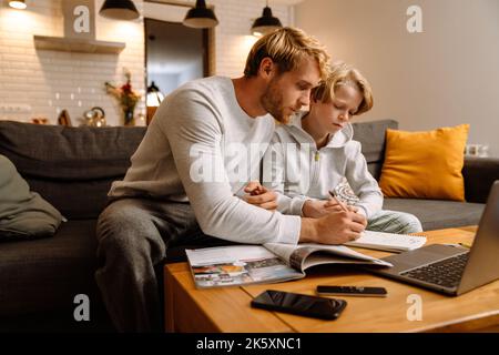 Ginger boy using laptop while doing homework with his father at home Stock Photo
