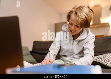 White ginger boy smiling and using laptop while doing homework at home Stock Photo