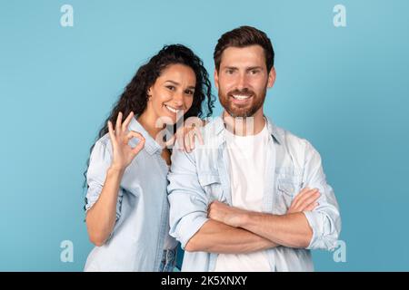Smiling confident young arabic lady and caucasian man with beard looking at camera, showing ok sign Stock Photo