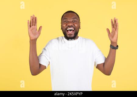 Excited Black Man Shouting In Joy Raising Arms, Yellow Background Stock Photo