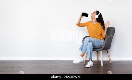 Happy woman singing on white, using smartphone and headphones Stock Photo