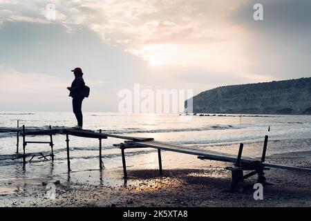 Traveller's silhouette on an old wooden pier at Zapallo Bay (Apollo bay). Episkopi, Limassol District, Cyprus Stock Photo