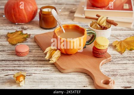 Aesthetics pumpkin latte in pumpkin cup. Seasonal breakfast with coffee and macaroons among pumpkins and winter cherry. Cozy autumn home. Stock Photo
