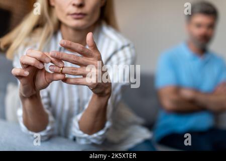 Unhappy middle aged european lady takes off ring, ignoring man during quarrel in living room interior Stock Photo