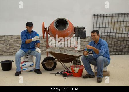 Image of two smiling construction workers on a construction site while having a beer during their lunch break. Moment of relaxation while working. Stock Photo