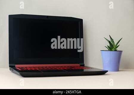 Open laptop black screen. Mockup for design. Flower pot in the trending color of 2022 Very Peri. An empty workplace without people. The concept of tec Stock Photo