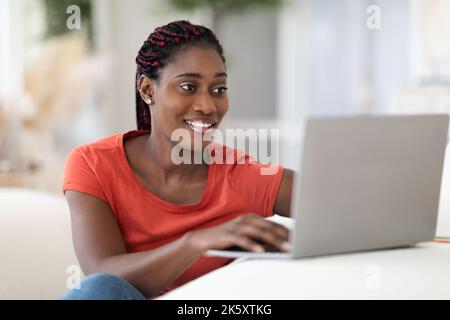 Beautiful Young Black Woman Using Laptop While Sitting At Desk At Home Stock Photo