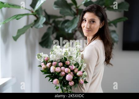 Positive woman holding a huge bouquet of flowers in her office. Birthday present smile. Stock Photo