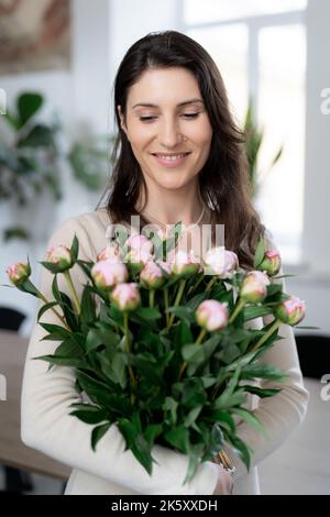 Positive woman holding a huge bouquet of flowers in her office. Birthday present smile. Stock Photo