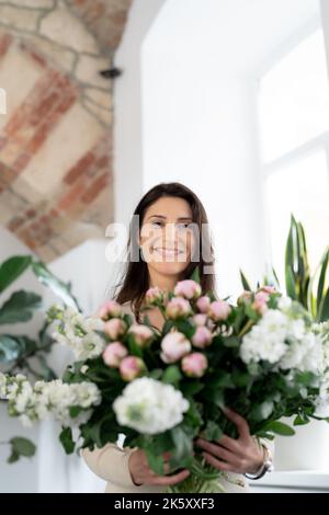 Positive woman holding a huge bouquet of flowers in her office. Birthday present smile. Stock Photo