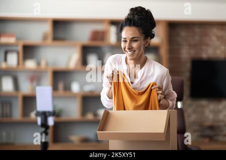 Cheerful young woman unpacking parcel and recording video Stock Photo