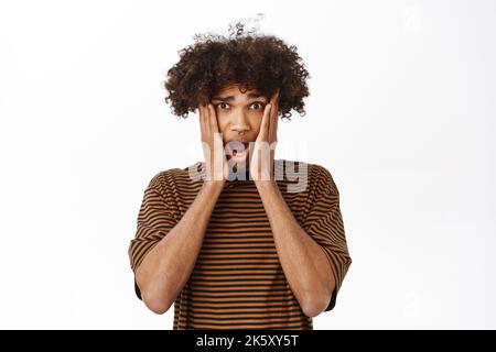 Portrait of hispanic guy looks with shocked face at camera, seeing smth terrible, reacting startled, standing over white background Stock Photo