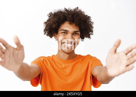 Close up portrait of smiling hispanic man reaching out his hands, stretching arms, holding something, standing over white background Stock Photo