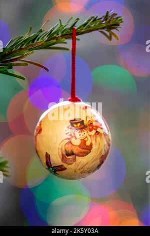 Single hand-made bauble hanging on the branch of a Christmas tree with out of focus fairy lights in the background