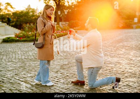 White man making proposal to his girlfriend with engagement ring during walking in autumn park Stock Photo