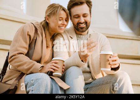 White romantic couple using cellphone and drinking coffee during date outdoors Stock Photo
