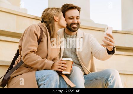 White romantic couple kissing and taking selfie on cellphone during date outdoors Stock Photo
