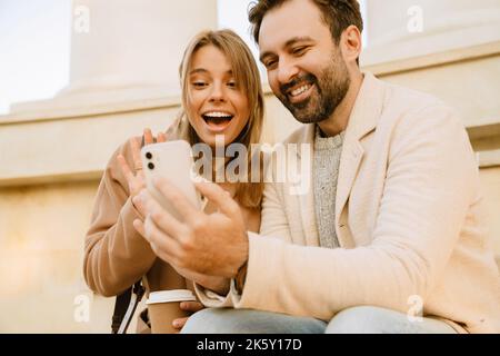 White romantic couple using cellphone and laughing during date outdoors Stock Photo