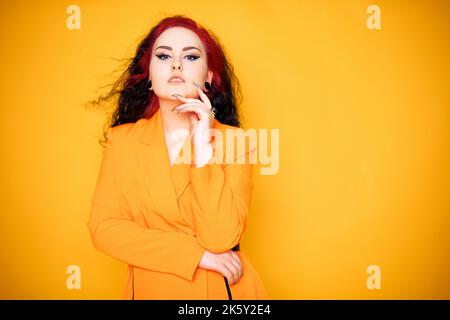 Beautiful girl on a yellow background. A brunette in an orange dress and long hair is posing, smiling, having fun. Summer photo woman in studio. Joy a Stock Photo