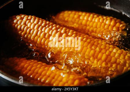 Orange juicy corn is boiled in water with salt. Corn in boiling water in a saucepan Stock Photo