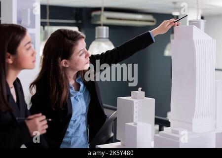 Real estate agency employees coworking, discussing building 3d model, brainstorming ideas in meeting. Architects thinking on city house construction project, looking at mock up building. Stock Photo