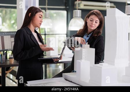 Architects discussing 3d apartment building model, engineers holding laptop, working on construction project in architecture office. Designers using software on tablet, engineering Stock Photo