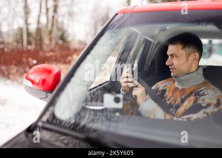 Side view portrait of adult man enjoying roadtrip in winter and taking photos from car, copy space Stock Photo