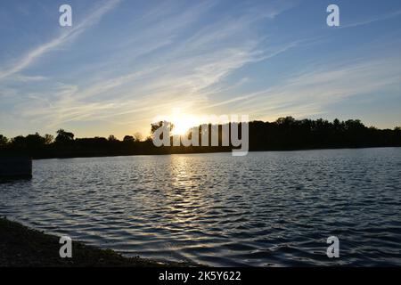 Sunset through trees over the view of a pond with a blue sky overhead. Stock Photo