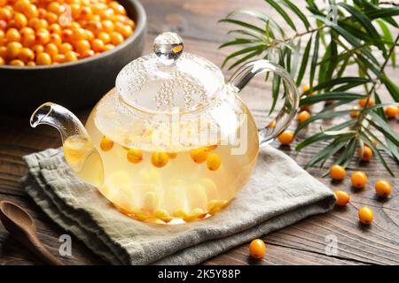 Glass tea kettle of healthy sea buckthorn tea, ripe sea buckthorn berries in a wooden bowl. Hot healthy tea to strengthen the immune system. Stock Photo