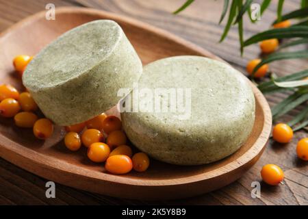 Solid shampoo pieces with sea buckthorn berries extract or homemade natural organic soap bars on wooden soap dish. Ripe sea buckthorn berries on woode Stock Photo