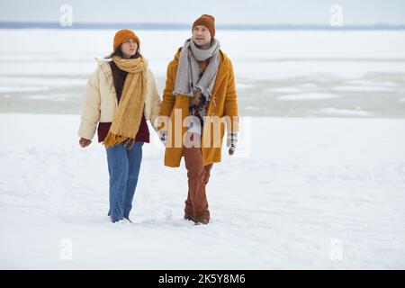 Full length portrait of young couple holding hands and walking towards camera in minimal winter landscape, copy space Stock Photo