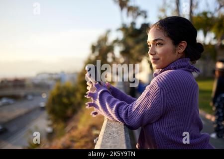 Contemplative woman with smart phone standing by railing Stock Photo