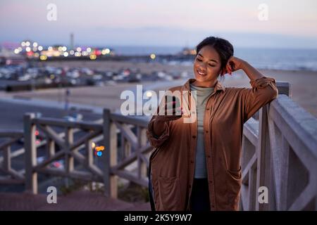 Smiling woman using smart phone leaning on railing Stock Photo