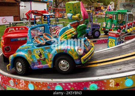 Fairground at Parsons Green, West London, UK; super-bright coloured rides, balloons, cars, trains and Spiderman Stock Photo