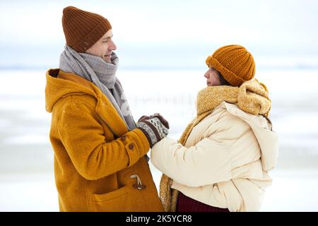 Side view portrait of romantic young couple holding hands in winter landscape, dating or proposal concept Stock Photo