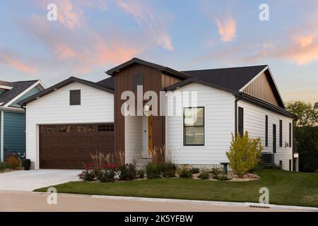 A beautiful modern home with white siding and wood accents, a yellow front door, and a brown garage door at sunset. Stock Photo