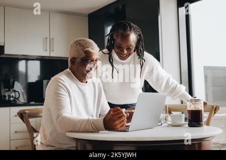 Retirement planning at home. Cheerful senior couple smiling happily while looking at a laptop screen. Happy mature couple researching their retirement Stock Photo