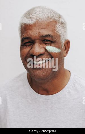 Happy mature man smiling at the camera with moisturizing cream on his face. Body positive senior man treating his aging skin with a nourishing beauty Stock Photo