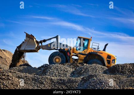 Volvo L220G wheel loader working on top of a mound at construction site, blue sky background. Stock Photo